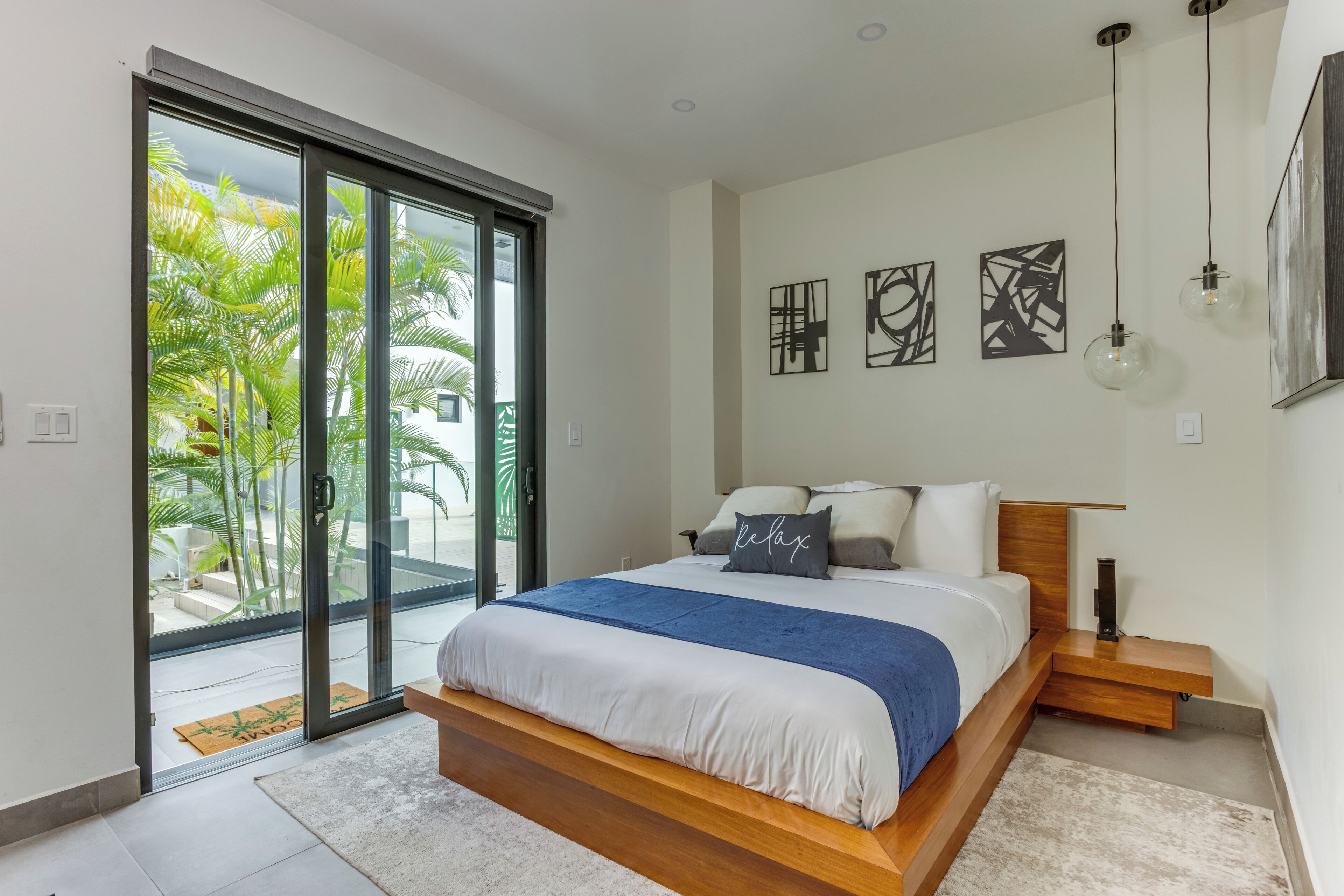 Une chambre à coucher moderne avec un grand lit, une porte-fenêtre coulissante donnant sur un balcon et des œuvres d’art abstraites accrochées au mur.