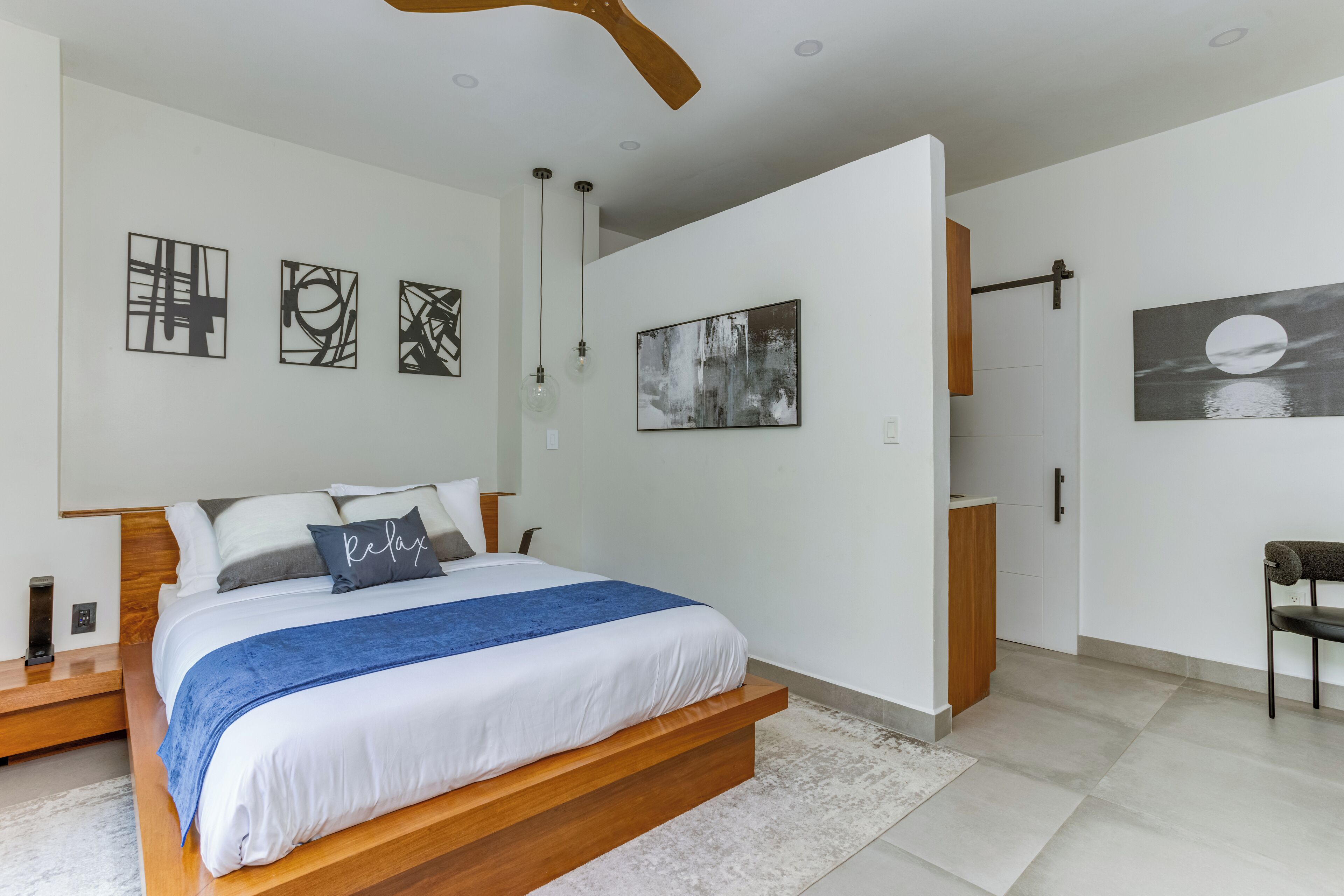 A modern bedroom with a wooden bed, a blue accent pillow, and abstract wall art.