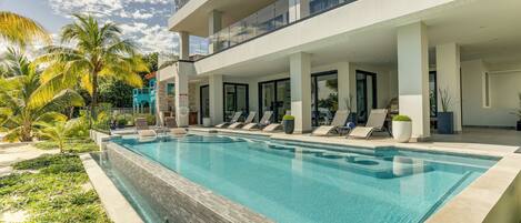 A modern hotel with a swimming pool, outdoor seating, and palm trees.