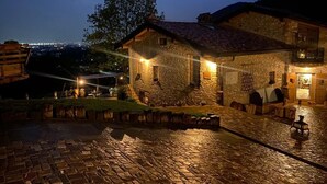 Edifici de pedra amb teulada d'estries, pati pavimentat i vista a la ciutat a l'hora del vespre.