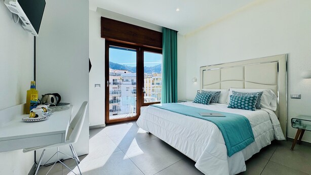 A modern hotel room with a bed, a desk, a TV, and a balcony with a city view. - Vera Gioia Rooms de Charme (Sorrento)