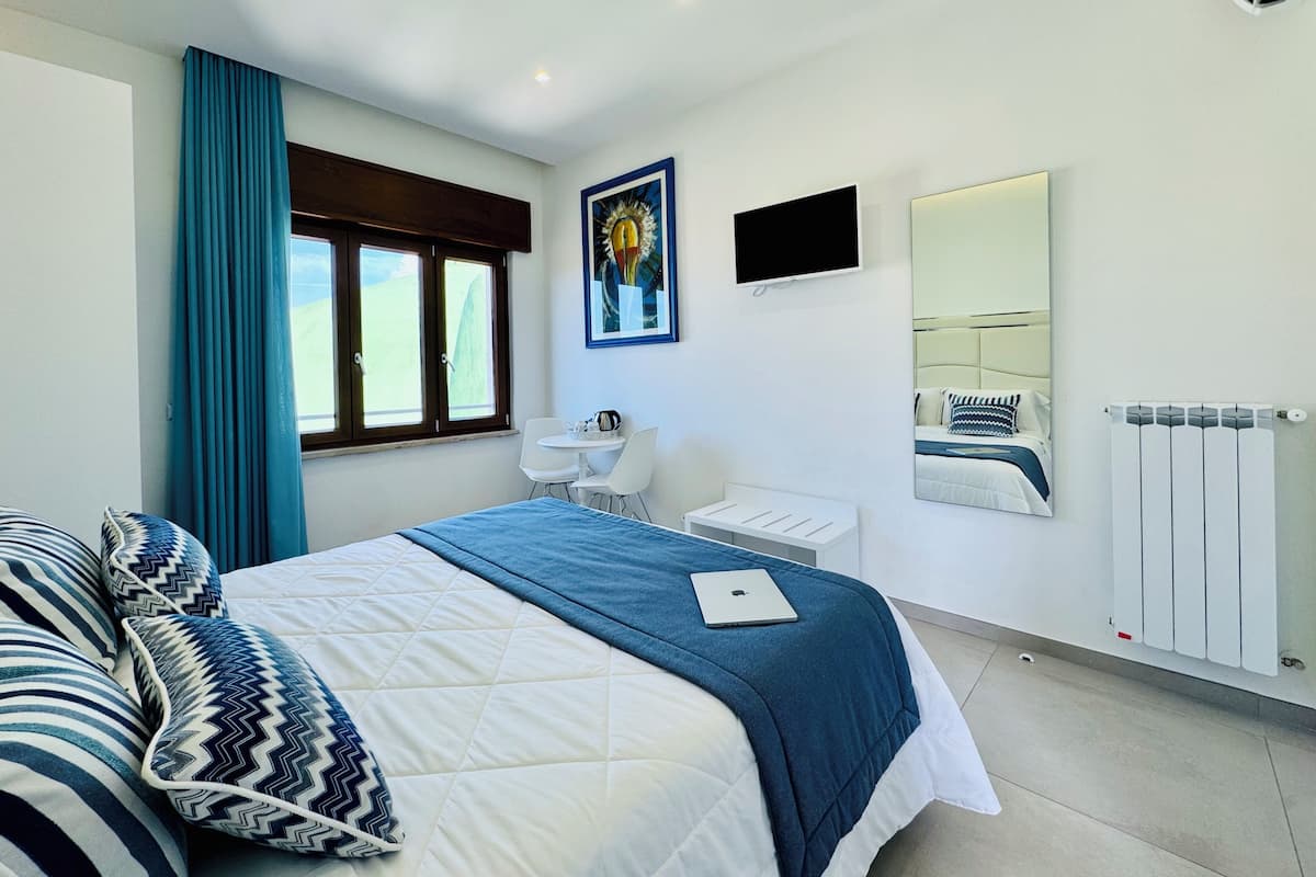 Une chambre moderne comprenant un lit, un bureau, une chaise, une télévision, un miroir et une fenêtre avec des rideaux.