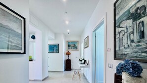 A hallway with white walls, tiled flooring, and framed artwork. There is a desk with a laptop and a vase of flowers. - Vera Gioia Rooms de Charme (Sorrento)