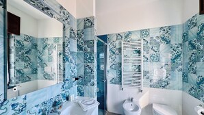 A bathroom with a white sink, a bidet, and a toilet, all against a blue and white patterned tile wall. - Vera Gioia Rooms de Charme (Sorrento)