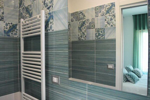 A bathroom with patterned tiles, a towel rack, and a mirror reflecting a bed with pillows. - Vera Gioia Rooms de Charme (Sorrento)