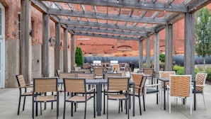 Un espace extérieur aménagé en terrasse, avec des tables et des chaises, une pergola et un mur de briques en arrière-plan.