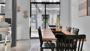 Un espace de bureau moderne avec une longue table en bois, des chaises noires et une porte en verre donnant sur un espace extérieur.