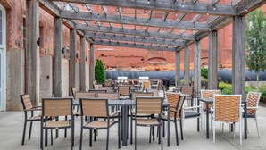 Un espace extérieur aménagé en terrasse, avec des tables et des chaises, une pergola et un mur de briques en arrière-plan.