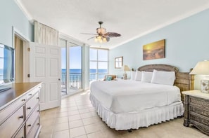 A bedroom with a large bed, a ceiling fan, a view of the ocean, and a door leading to a balcony.