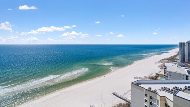 A beach view with a clear sky and ocean. There are buildings along the shore. - Palacio 303 (Pensacola)