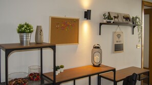 Une pièce avec une table en bois, un tableau d’affichage en liège orné d’épingles colorées, une étagère murale décorative et un luminaire fixé au mur.