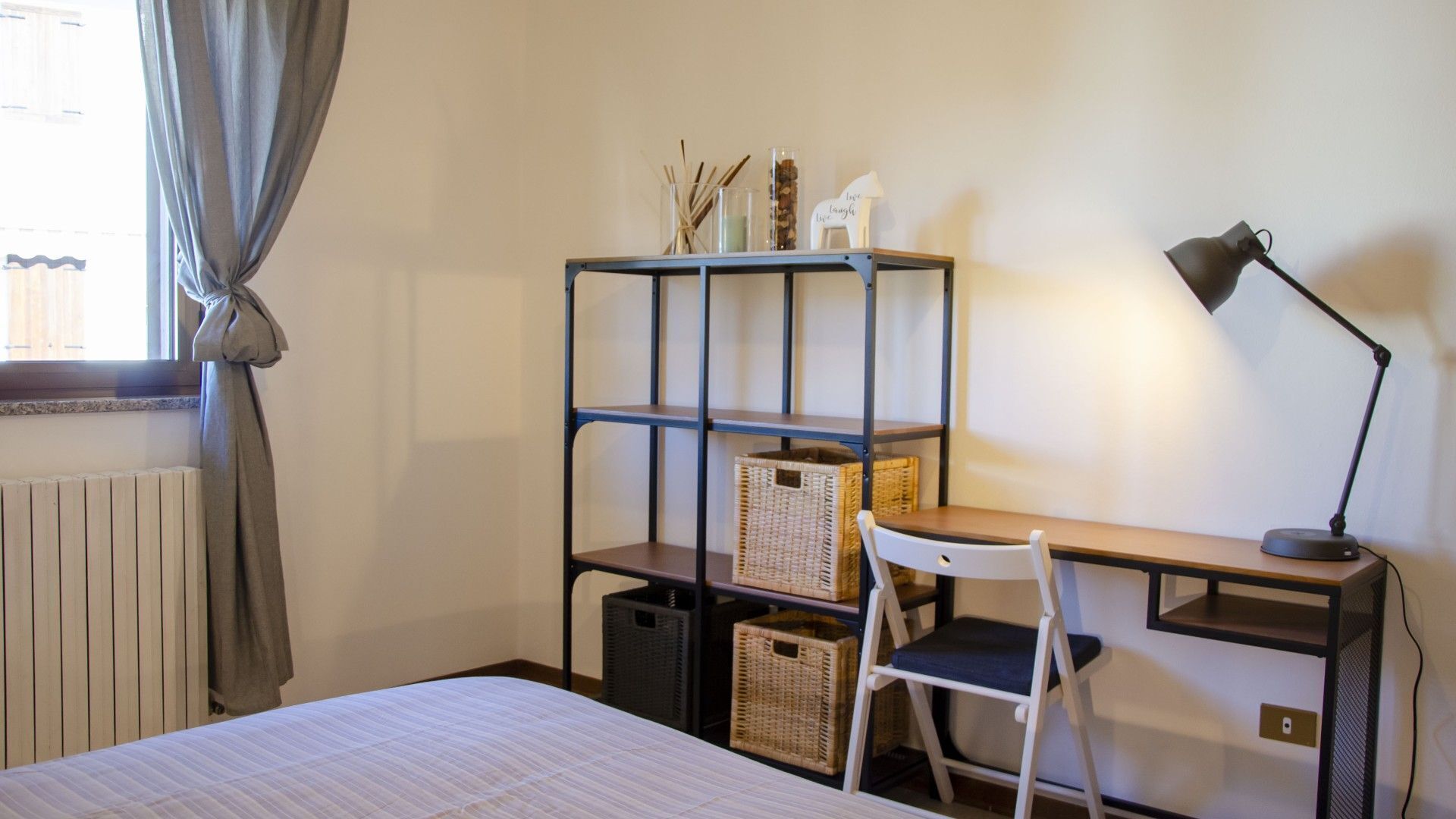 A bedroom with a bed, a desk with a chair, a bookshelf, and a lamp.