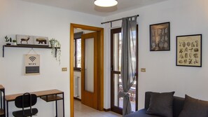 Une pièce comprenant un bureau, une chaise, un canapé, une porte donnant sur une autre pièce et un mur orné de reproductions botaniques encadrées.