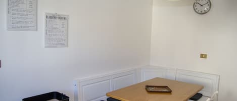 A small dining area with a wooden table and white bench seating. There are two wall-mounted signs with recipes.