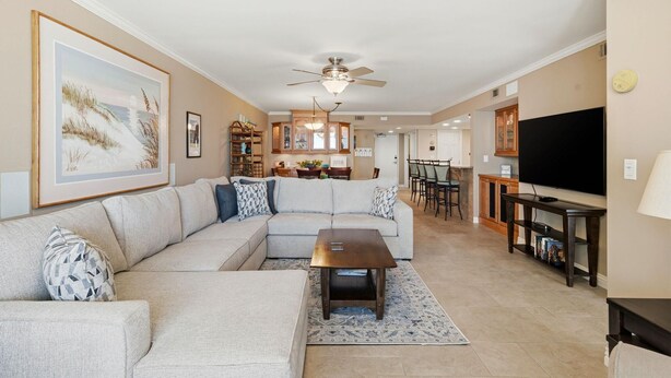 A living room with a sectional sofa, a coffee table, a TV, and a dining area in the background. - Seaspray East 624-gulf Front (Pensacola)