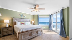 Une chambre avec un lit, des tables de chevet, un ventilateur de plafond et une vue sur l’océan.