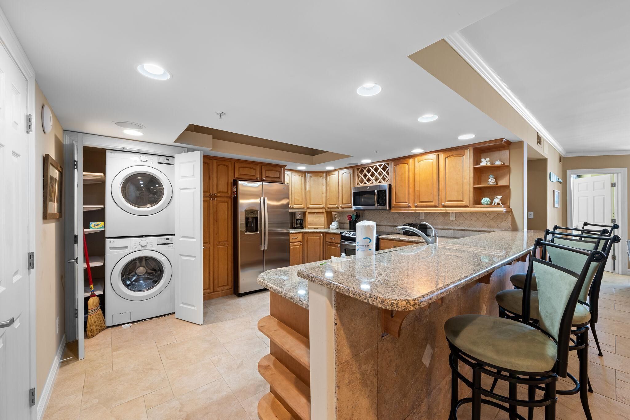 A modern kitchen with a built-in washer and dryer, stainless steel appliances, and a granite island with bar stools.