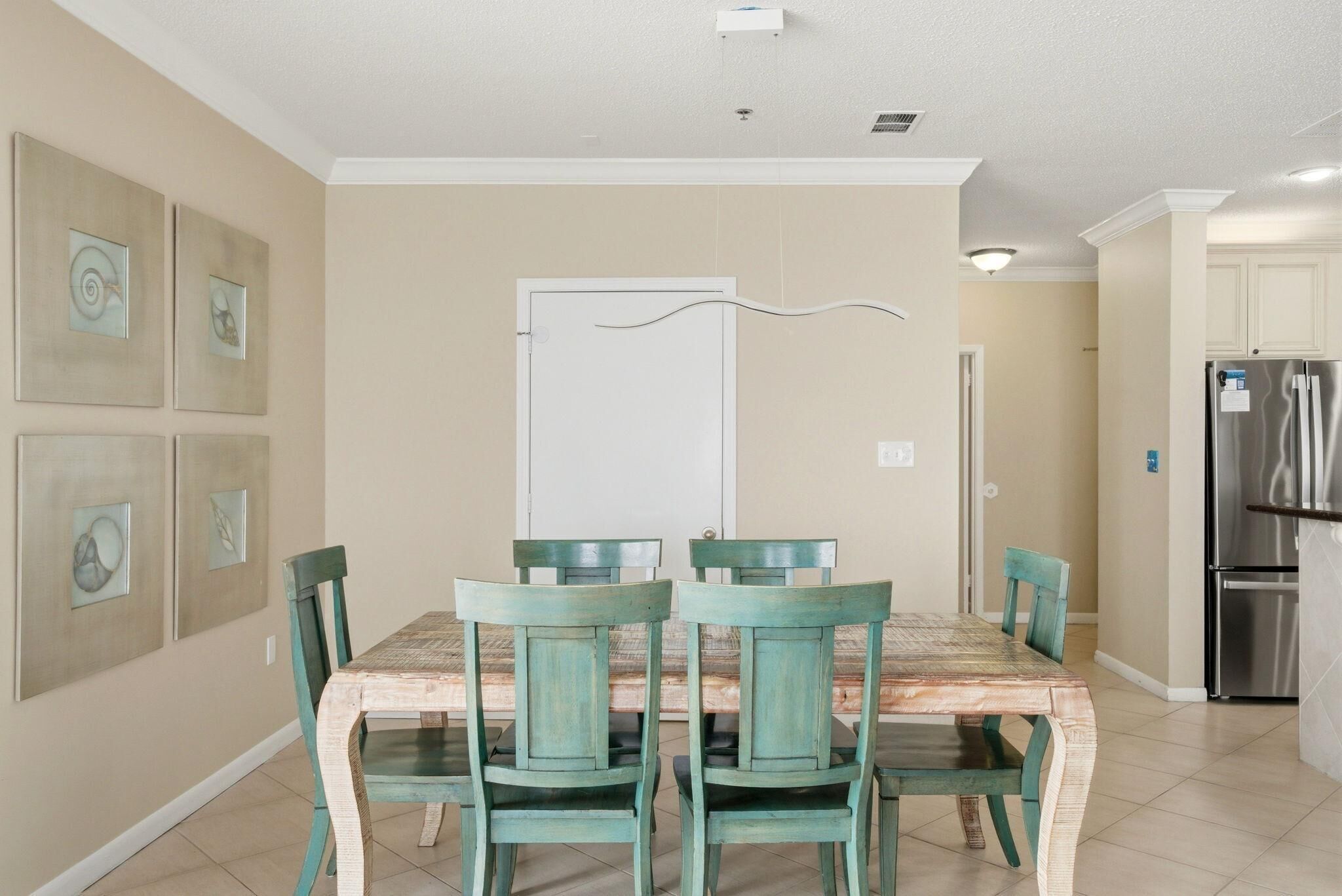 A dining area with a table and chairs, a kitchen with a refrigerator, and wall art.