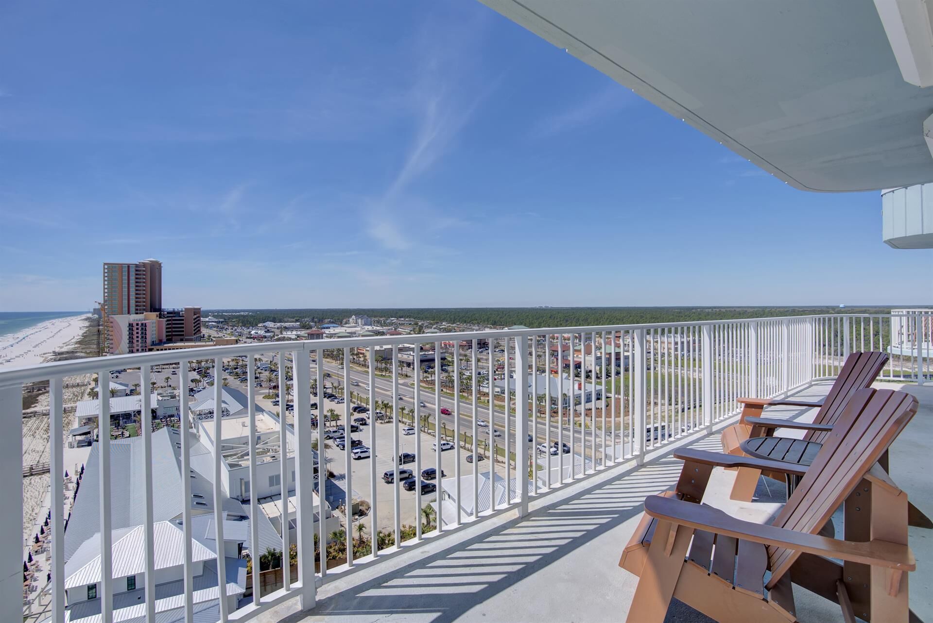 Ein Balkon mit weißen Geländern, der auf einen Parkplatz und einen Strand blickt.