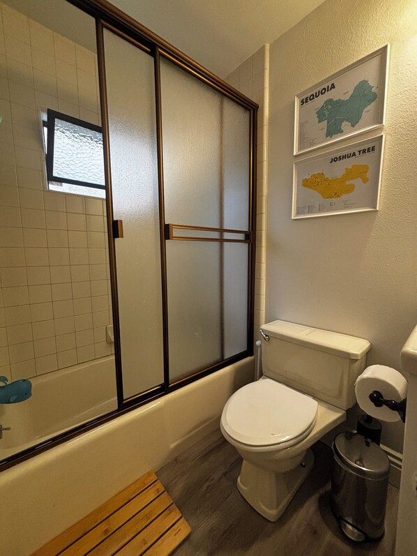 A bathroom with a toilet, a shower with a glass door, and two framed maps on the wall.