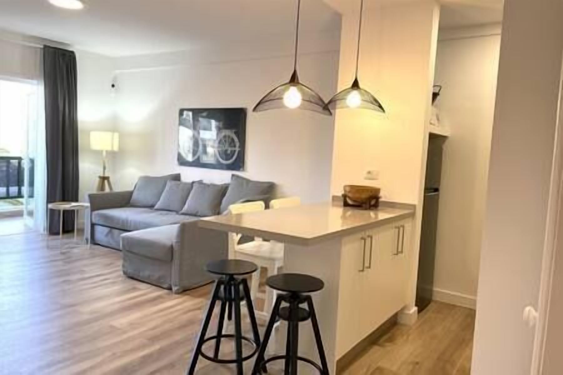A modern living room with a sofa, a coffee table, and a kitchen area with a counter and stools.