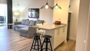 A modern living room with a sofa, a coffee table, and a kitchen area with a counter and stools. - Alcalá on the beach with stunning views of Teide (Alcalá)