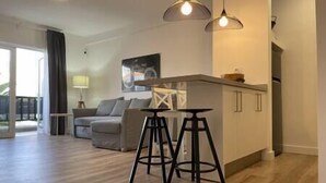A modern living room with a sofa, a dining area with stools, and a kitchen area with cabinets. - Alcalá on the beach with stunning views of Teide (Alcalá)