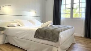 A neatly made bed with white linens and a gray throw blanket, a bedside table with a lamp, and a window with curtains. - Alcalá on the beach with stunning views of Teide (Alcalá)