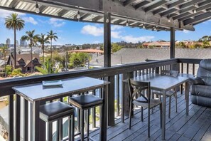 Eine überdachte Terrasse im Freien mit Tisch und Stühlen, mit Blick auf eine Wohngegend mit Palmen und Häusern.