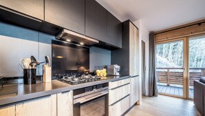 A modern kitchen with a built-in oven, a gas stove, and a large window overlooking a wooden deck.
