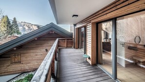 A wooden balcony with a view of mountains, a glass door, and a small table.