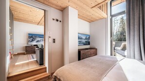 Ein modernes Schlafzimmer mit einem großen Bett, Holzboden, einer Schiebetür, die auf einen Balkon führt, und zwei an der Wand befestigten Fernsehern.
