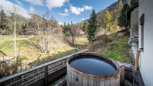 Ein Holzbottich auf einer Terrasse mit Blick auf eine gebirgige Landschaft und ein Haus im Hintergrund.