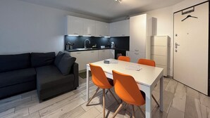 Een moderne keuken met witte kastjes, een zwart aanrecht en een eethoek met een witte tafel en oranje stoelen.