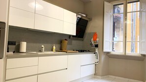 A modern kitchen with white cabinets, a stainless steel range hood, a window with a view of the outside, and a tiled floor. - Rocco's Home at the Colosseum (Roma)