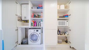 A compact laundry room with a built-in washer and dryer, shelves with cleaning supplies, and a microwave. - Rocco's Home at the Colosseum (Roma)