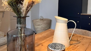 Une table en bois sur laquelle se trouvent un vase en verre rempli de fleurs, un pichet en métal, un salier et un bol décoratif.