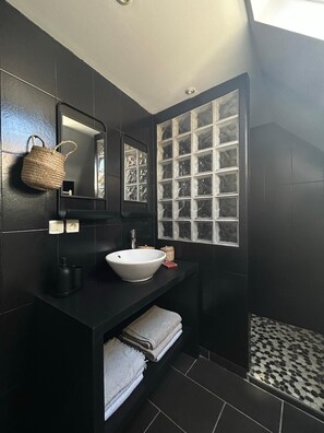 A modern bathroom with a black vanity, a white sink, a large mirror, and a window with frosted glass.