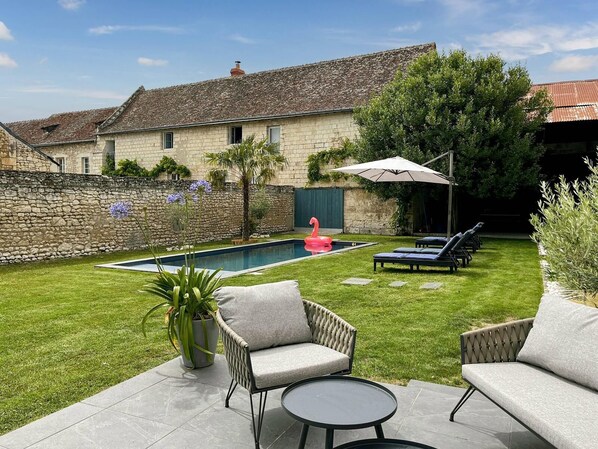 A stone house with a swimming pool, outdoor seating, and a well-maintained lawn.