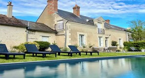 A poolside area with lounge chairs, a swimming pool, and a building with stone walls and multiple chimneys. - South Touraine village house with swimming pool near Chinon Azay 10 p (Tavant)