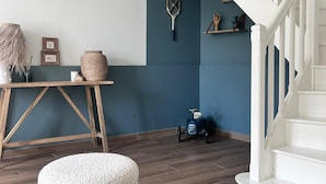 Un salon moderne avec une table en bois, un pouf blanc, un mur bleu et un escalier blanc.