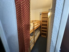 Une petite pièce avec un lit superposé, une étagère en bois et un rideau à motifs.