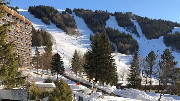 A snow-covered mountain slope with a ski lift, a building with balconies, and a clear sky.