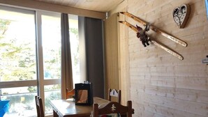 A wooden interior with a dining table, chairs, a ceiling light fixture, and a ski rack with skis and a heart-shaped decoration.