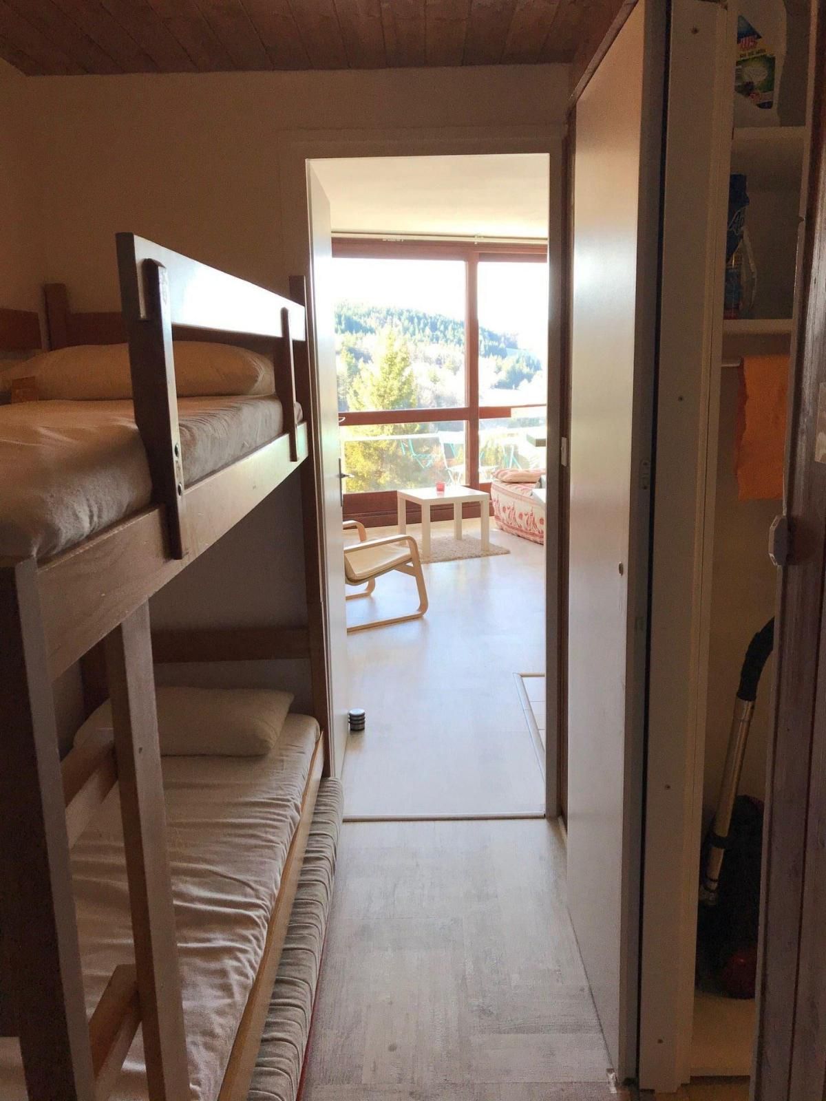 A room with a bunk bed, a small table, and a chair. There is a door leading to a balcony with a view of trees and hills.