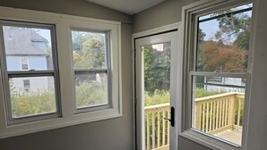 Une pièce avec deux fenêtres, une porte et une vue sur une terrasse en bois et des arbres.