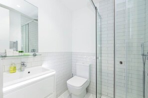 A modern bathroom with a glass-enclosed shower, a white sink, and a toilet. - Stylish Studio Retreat in Trendy Marylebone (London)