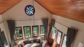 Uma sala de estar ampla com pé direito alto, grandes janelas, lareira e um lustre.