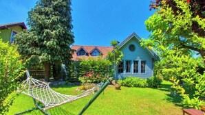 Uma casa com um jardim bem cuidado, uma rede e um banco de madeira.