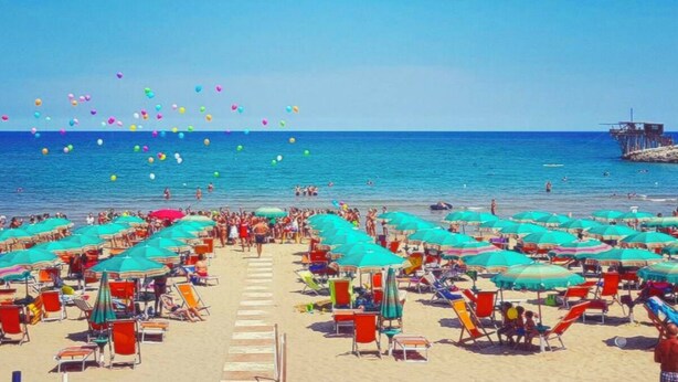 Una spiaggia con file di sedie a sdraio e ombrelloni, una torretta per i bagnini e un cielo azzurro.